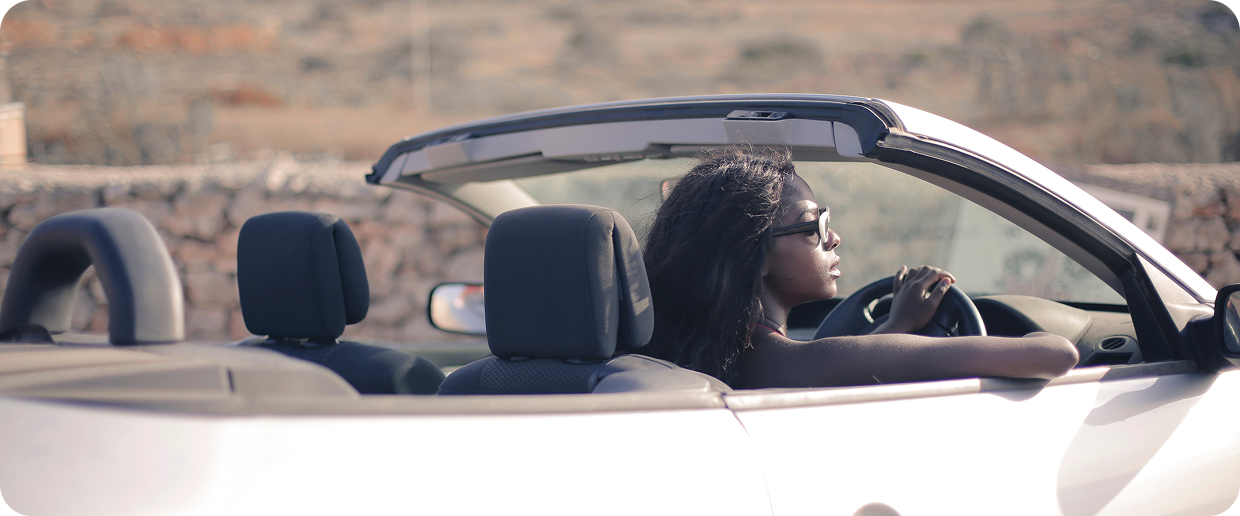 African driver enjoying a SAGLEV electric convertible vehicle on a scenic coastal road with stone walls and hills in the background
